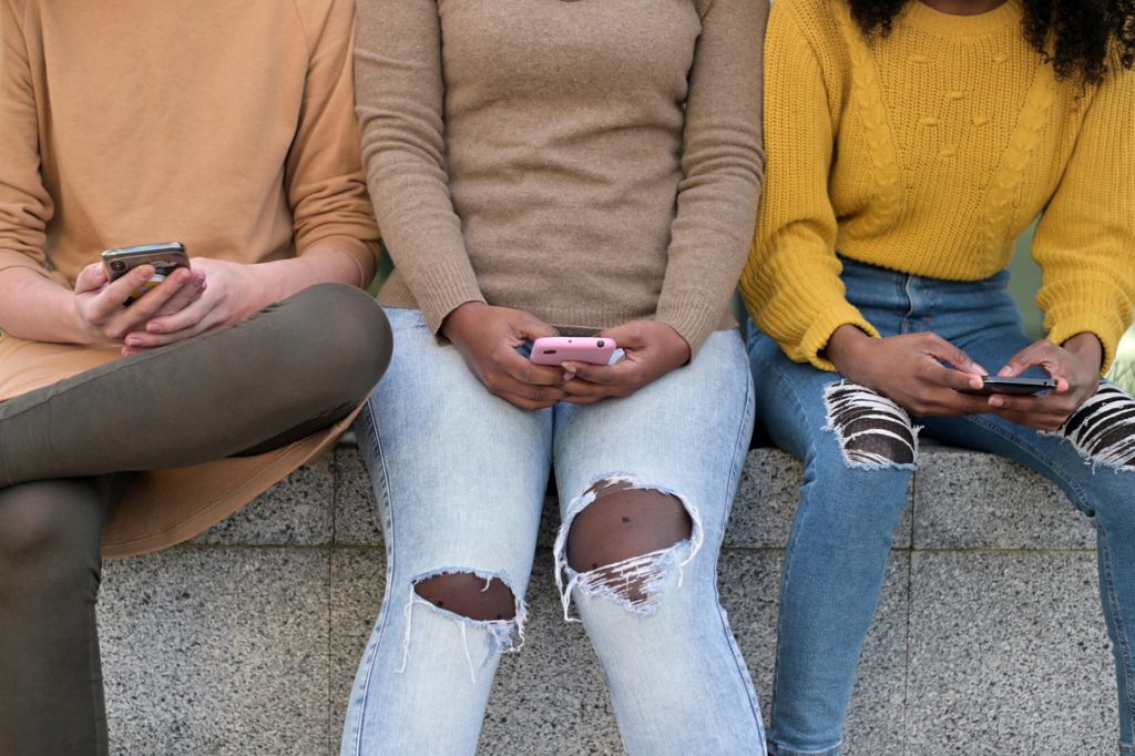 Meisjes zitten te appen op een muurtje